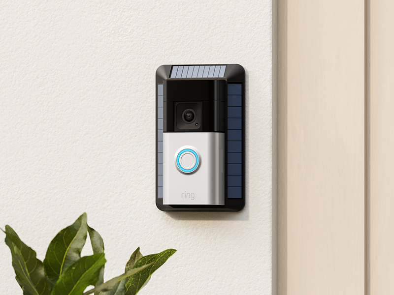 A Ring battery doorbell on a black solar charger mounted onto a beige wall.