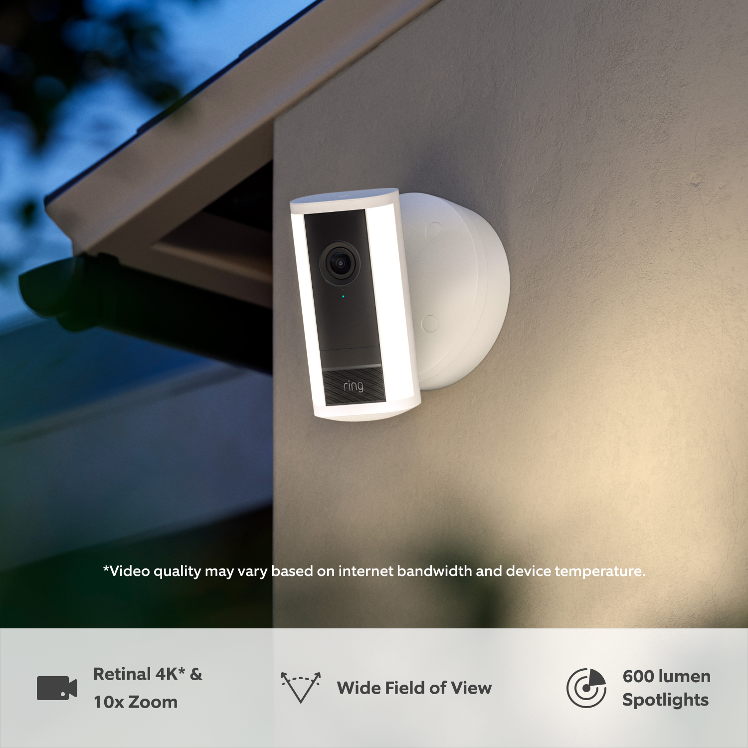 Spotlight Camera Pro (2nd Gen) (Featuring Retinal 4K) - Wired:White Ring Spotlight Cam Pro (2nd Gen) attached to a wall at dusk in the rain with built-in LED spotlights illuminated