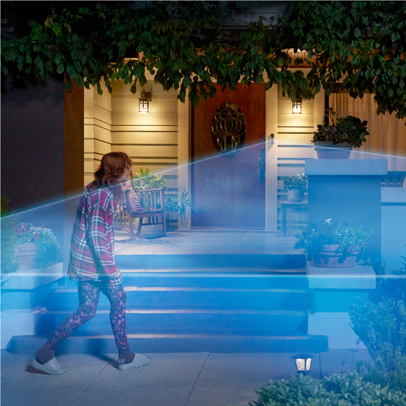 A person walks into a driveway covered in a blue laser graphic extending out from a Ring Wired Doorbell Pro mounted to the house.