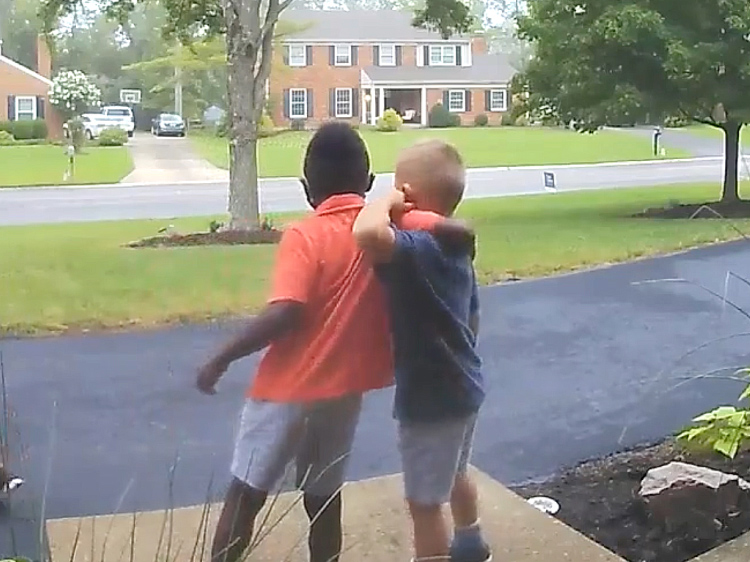 Two young boys give each other a hug from the side in a front yard.