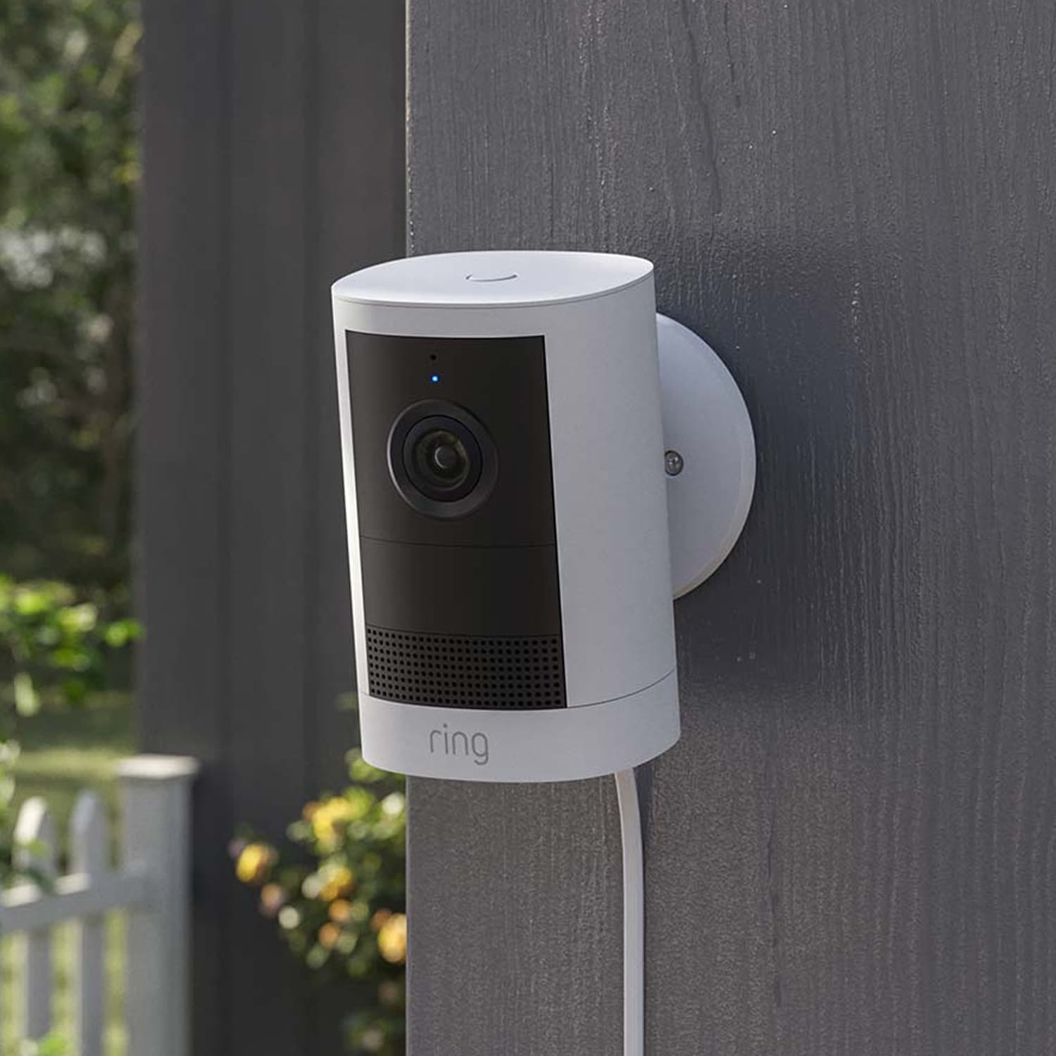Outdoor Cam (Newest Model)  - Plug-In:White Outdoor Cam (2nd Gen) mounted to a wall. Power cord stretches down the wall from the camera base.