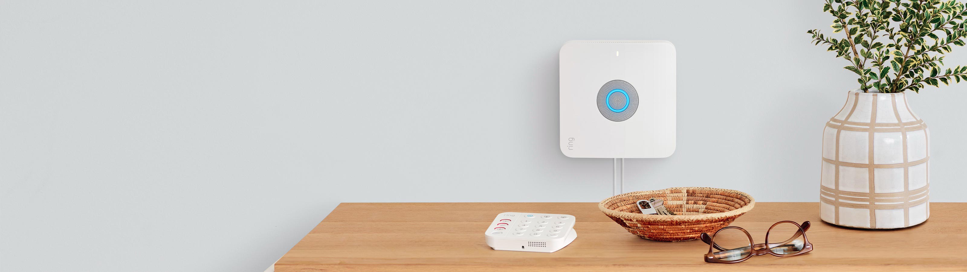 Alarm Pro Base Station mounted to a wall with the Keypad on a console next to a pair of glasses, a plant, and a small basket with keys in it.