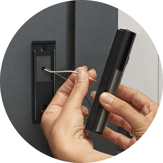 Close-up of hands installing a Wired Doorbell Pro (2nd Gen), showing the placement of the device against a dark doorframe surface for mounting.