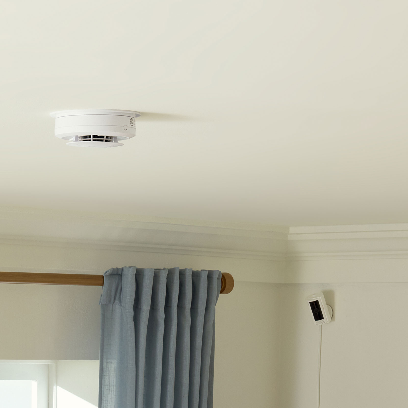 Smoke & CO Listener Alarm Bundle - A white Ring Alarm Smoke and CO Listener mounted on a ceiling next to a smoke detector near the front door of a home.