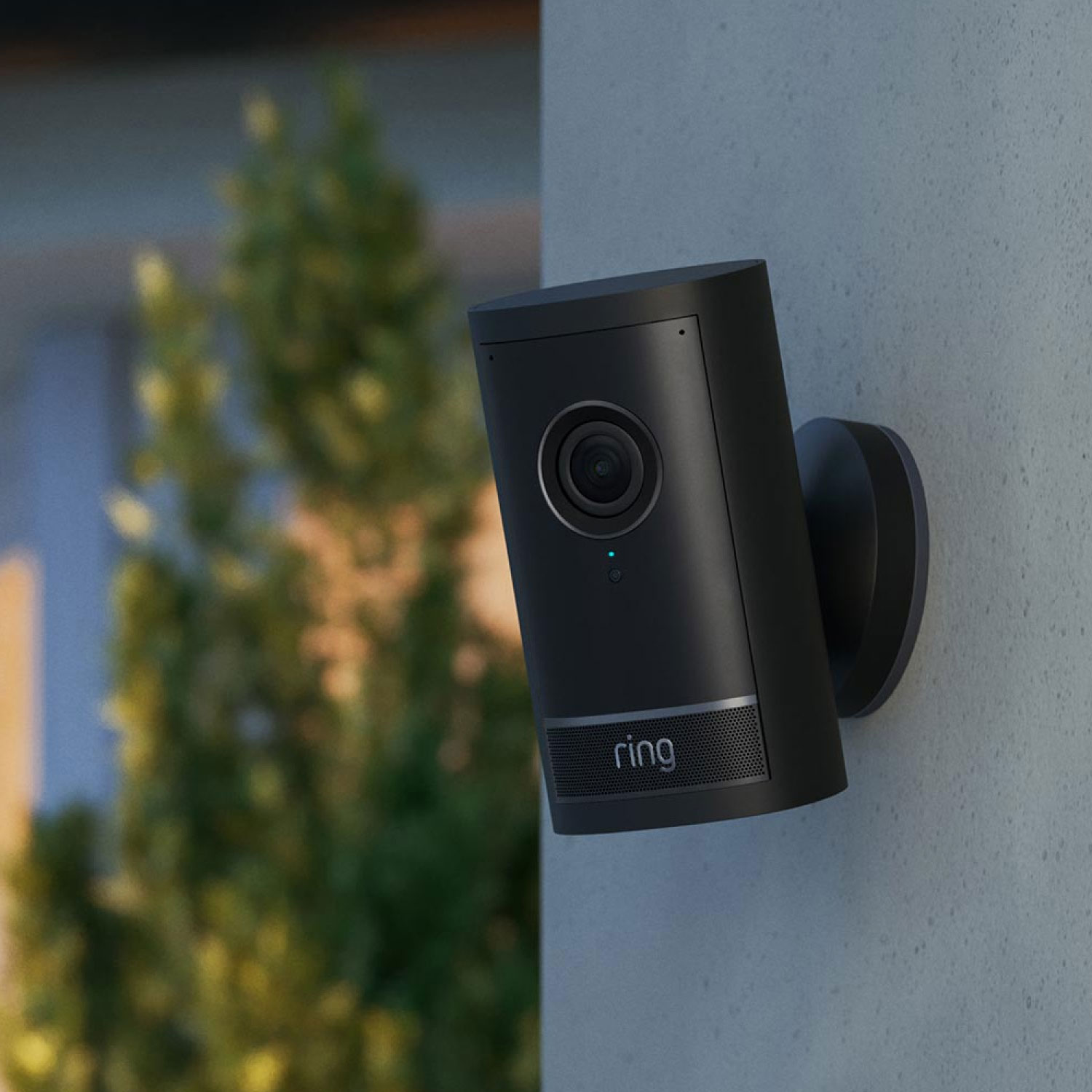 PoE+ Converter Mount - Black Outdoor Cam Pro mounted on a stone exterior wall using a black PoE plus Converter Mount with green foliage in the background.