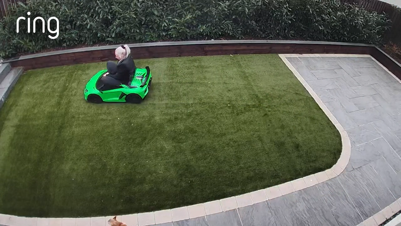 Kathleen rides an electric Lamborghini in the garden with Boo the dog