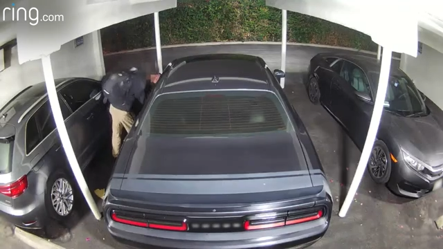 A man is seen peeping into vehicles. The siren is triggered and he leaves the carport.