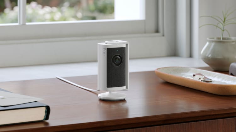 Indoor Cam 4K on a wooden desk near a plant, bowl, and book, with a rainy window in the background.