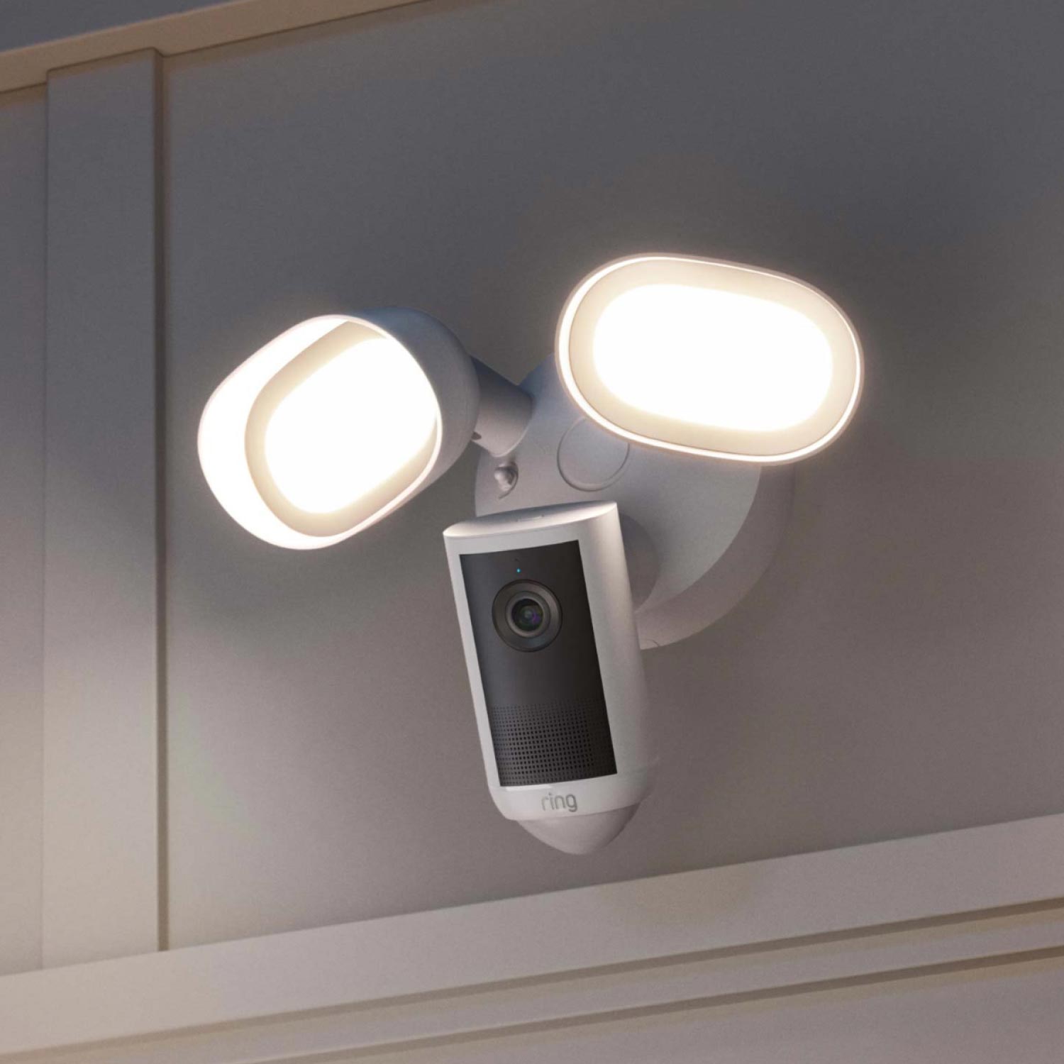 Floodlight Cam 4K Plus - Wired:Outdoor wall-mounted Ring floodlight with dual bright LED lamps and an integrated camera, shown powered on at dusk.