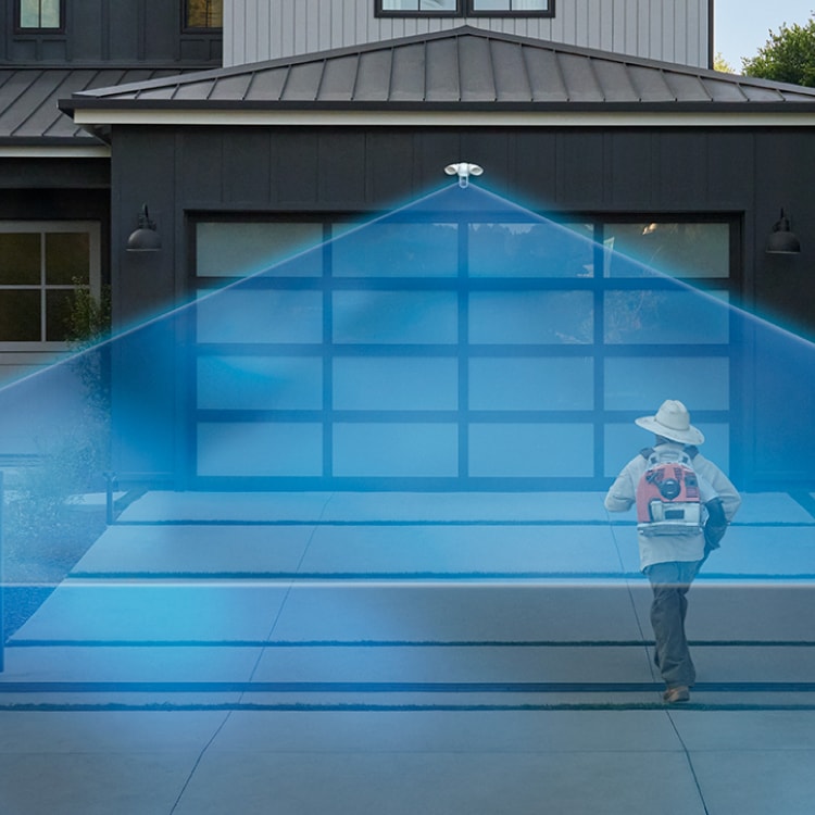 A landscaper walks into a driveway covered in a blue laser graphic extending out from a Ring Floodlight Cam Pro (2nd Gen) mounted to the house.
