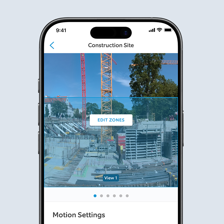 Smartphone screen showing a construction site camera view with cranes, framing, and an “Edit Zones” button in the app.