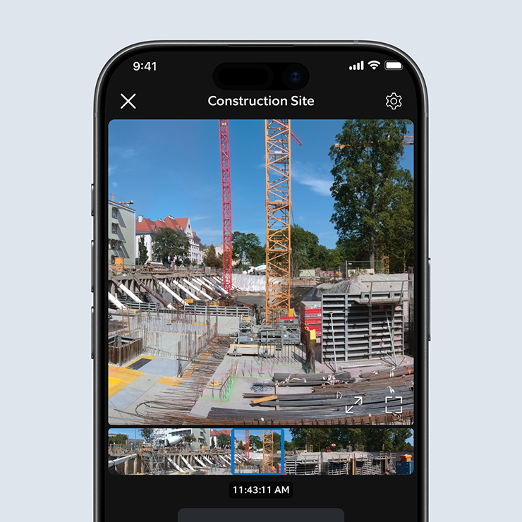 Smartphone screen showing a live view of a construction site with cranes, scaffolding, and materials under a clear blue sky.