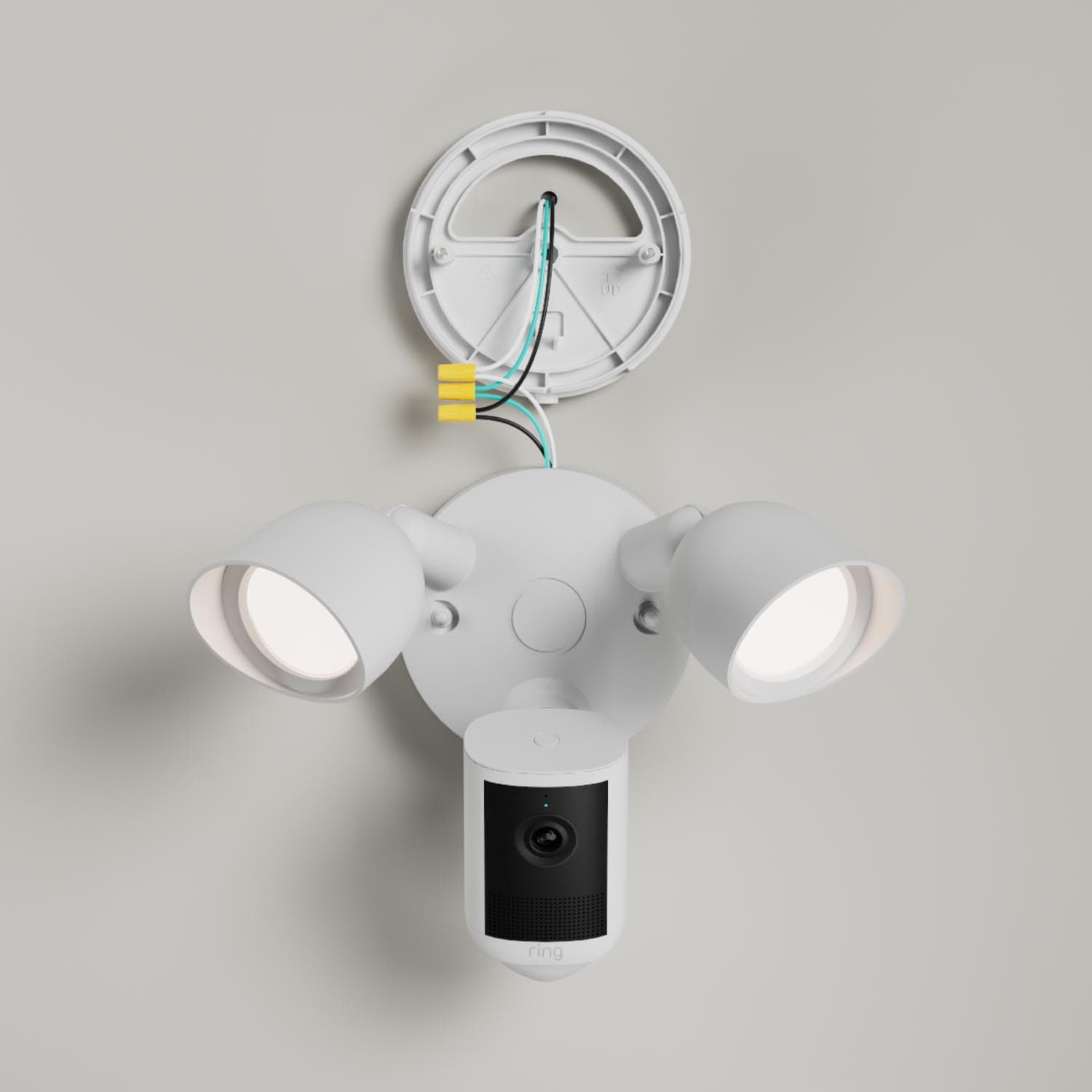 Floodlight Cam - White wall-mounted floodlight with two lit lamps and an integrated camera below, showing exposed wiring during installation.