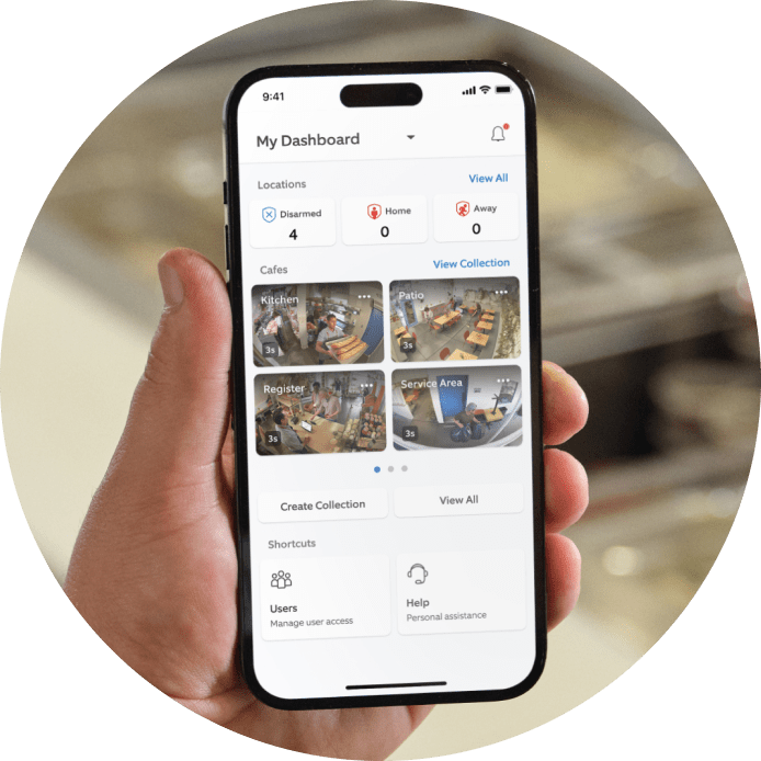 Hand holding smartphone displaying security dashboard with cafe surveillance cameras for kitchen, patio, register, and service area.