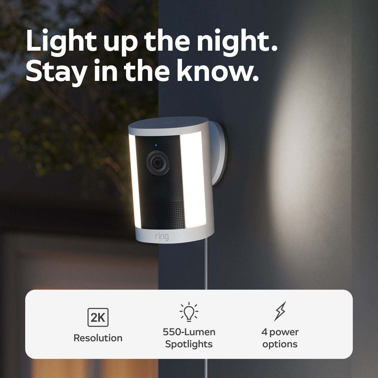 Spotlight Cam 2K - Plug-In:Wall-mounted Ring security camera with dual vertical LED spotlights glowing at night, promoting 2K resolution and four power options.