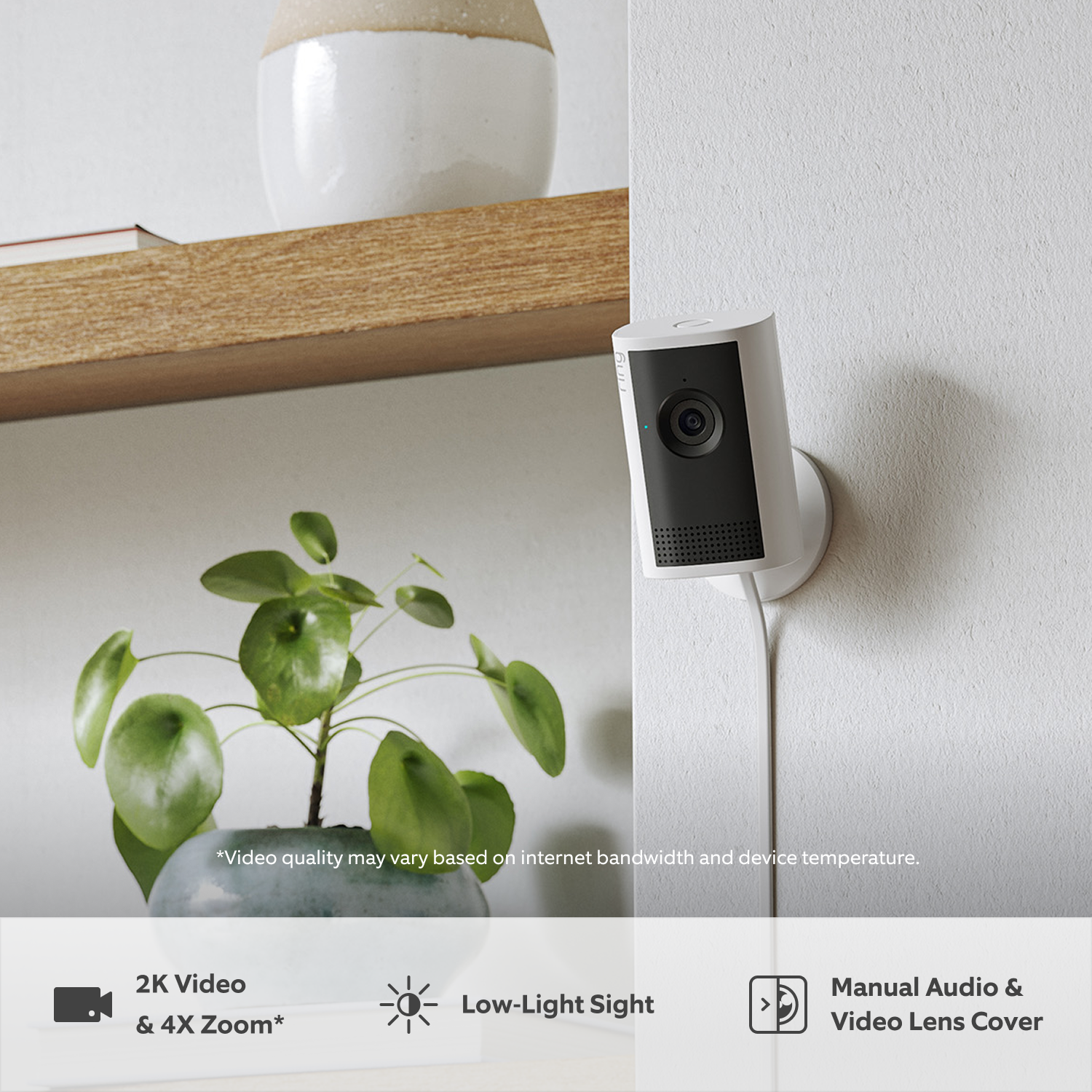 Indoor Camera Plus (Featuring Retinal 2K) - A white Indoor Cam Plus mounted on a wall next to a wooden shelf. Below the shelf is a small plant in a blue-grey pot.
