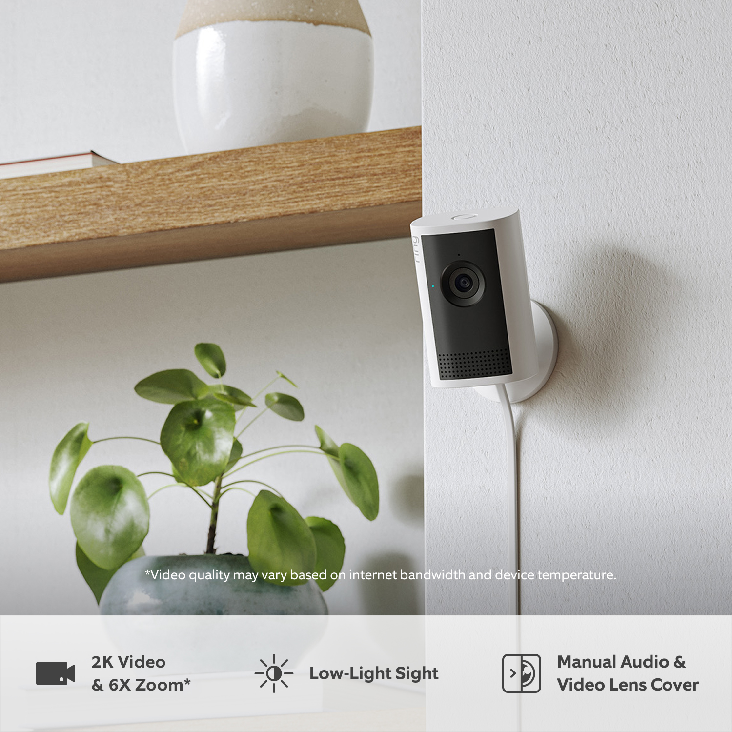 Indoor Camera 2K Plus - A white Indoor Cam Plus mounted on a wall next to a wooden shelf. Below the shelf is a small plant in a blue-grey pot.