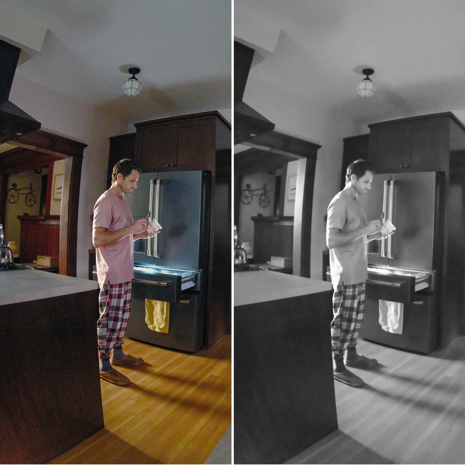 View of a home kitchen through an indoor security camera, showing a man in pajamas standing by a refrigerator eating ice cream at night.