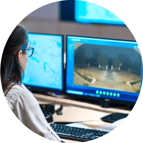 A security professional monitoring live camera footage on dual screens in a surveillance center.