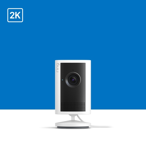 White Ring indoor camera on a stand against a blue background, labeled 2K, showing a front lens and speaker grille with power cable.