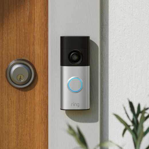 Sleek video doorbell mounted on a stucco wall, black and silver body with a glowing blue ring button and camera lens above.