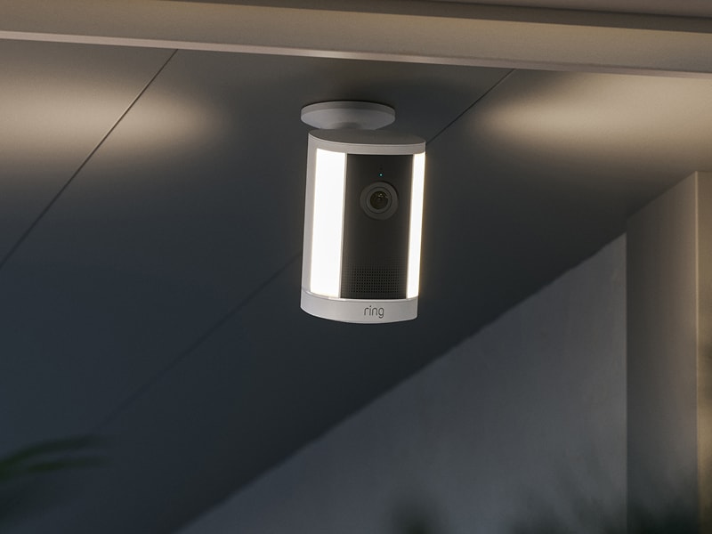 Ceiling-mounted Ring security camera with vertical LED lights, shown at dusk under an overhang.