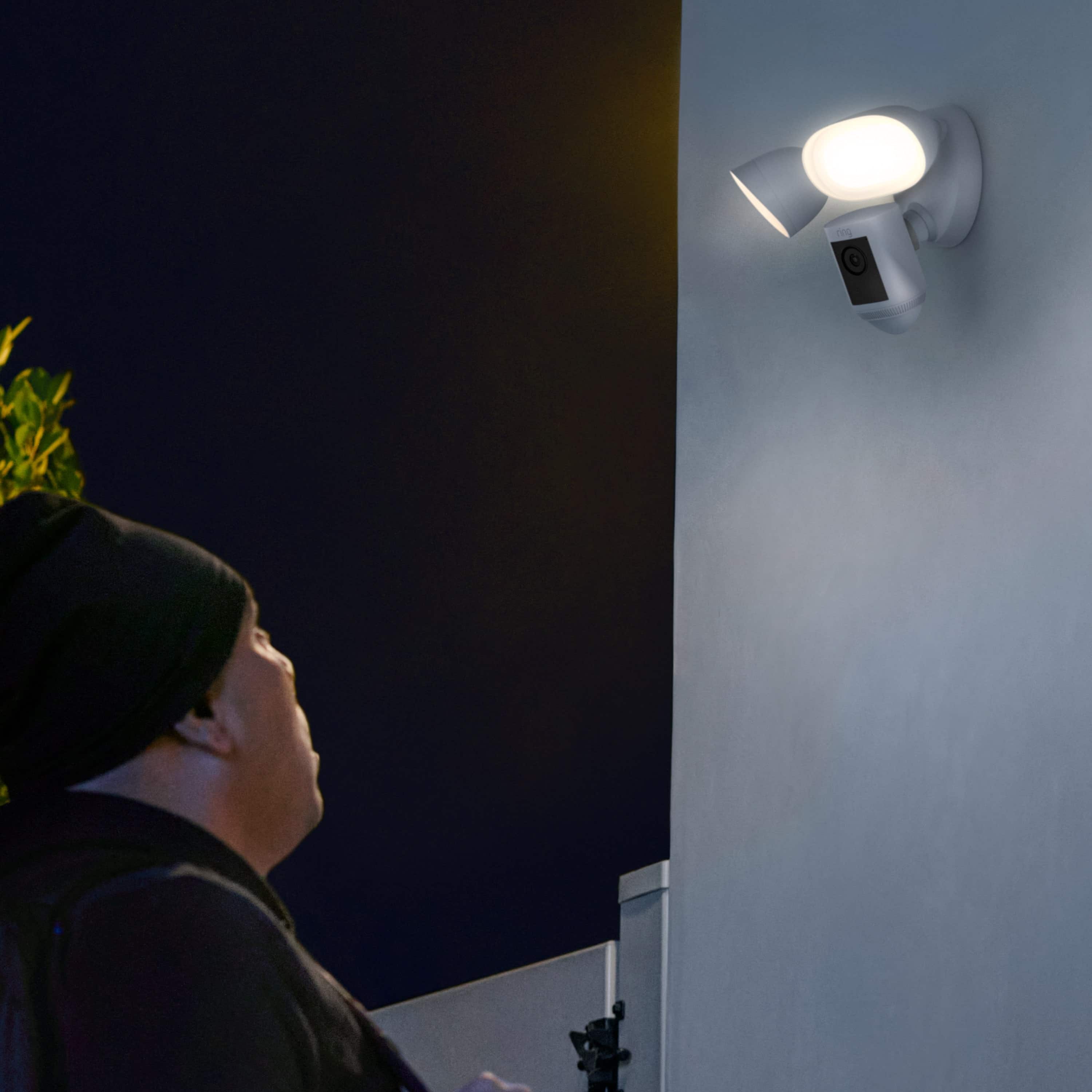 Floodlight Cam Pro (Plug-In) - Outside a home at night, a Floodlight Cam Pro shines light on a person dressed in black, who is looking up at the camera.