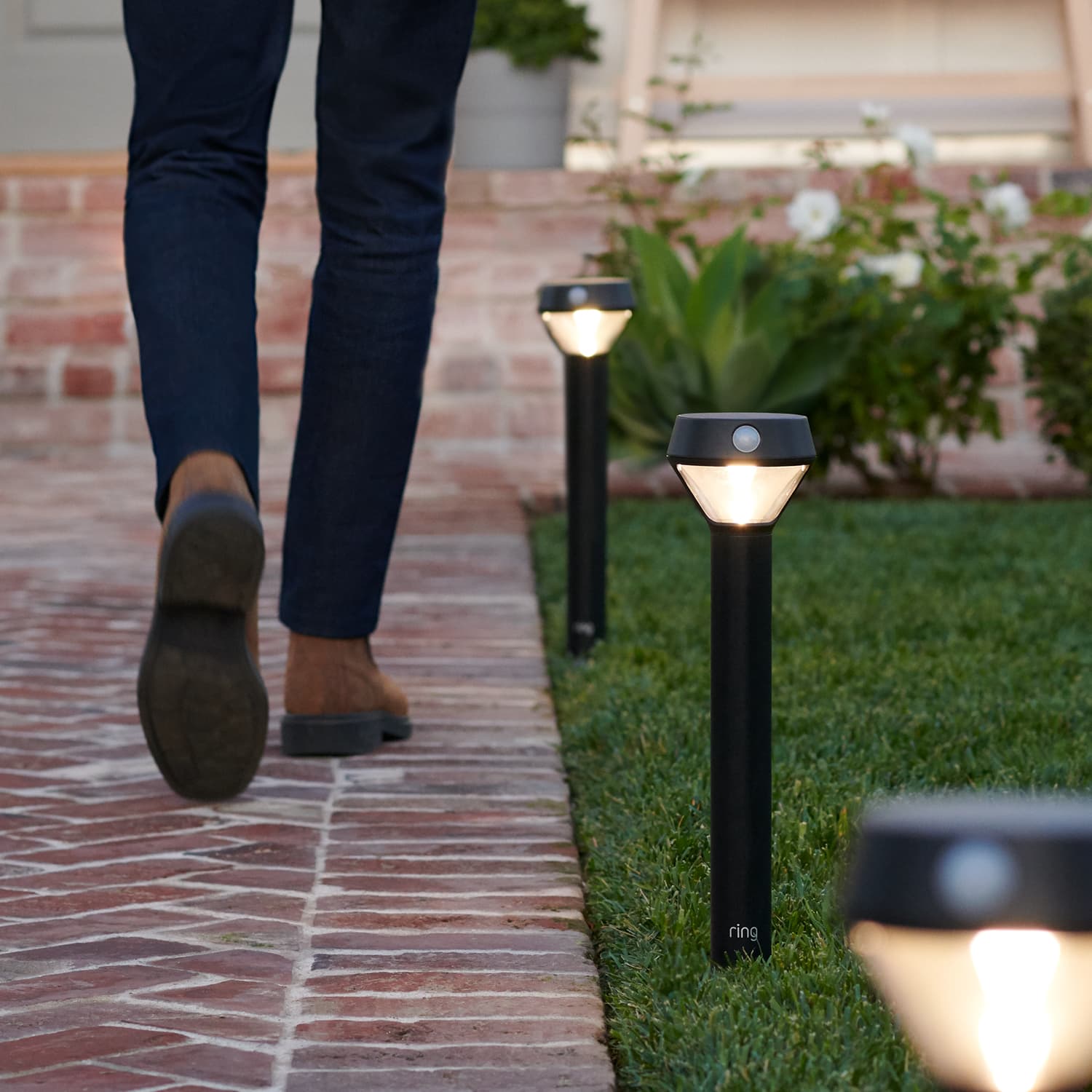 Smart Lighting Solar Pathlight - 3 Solar Pathlights are illuminated along a brick pathway while a person is walking towards the front door of a home.