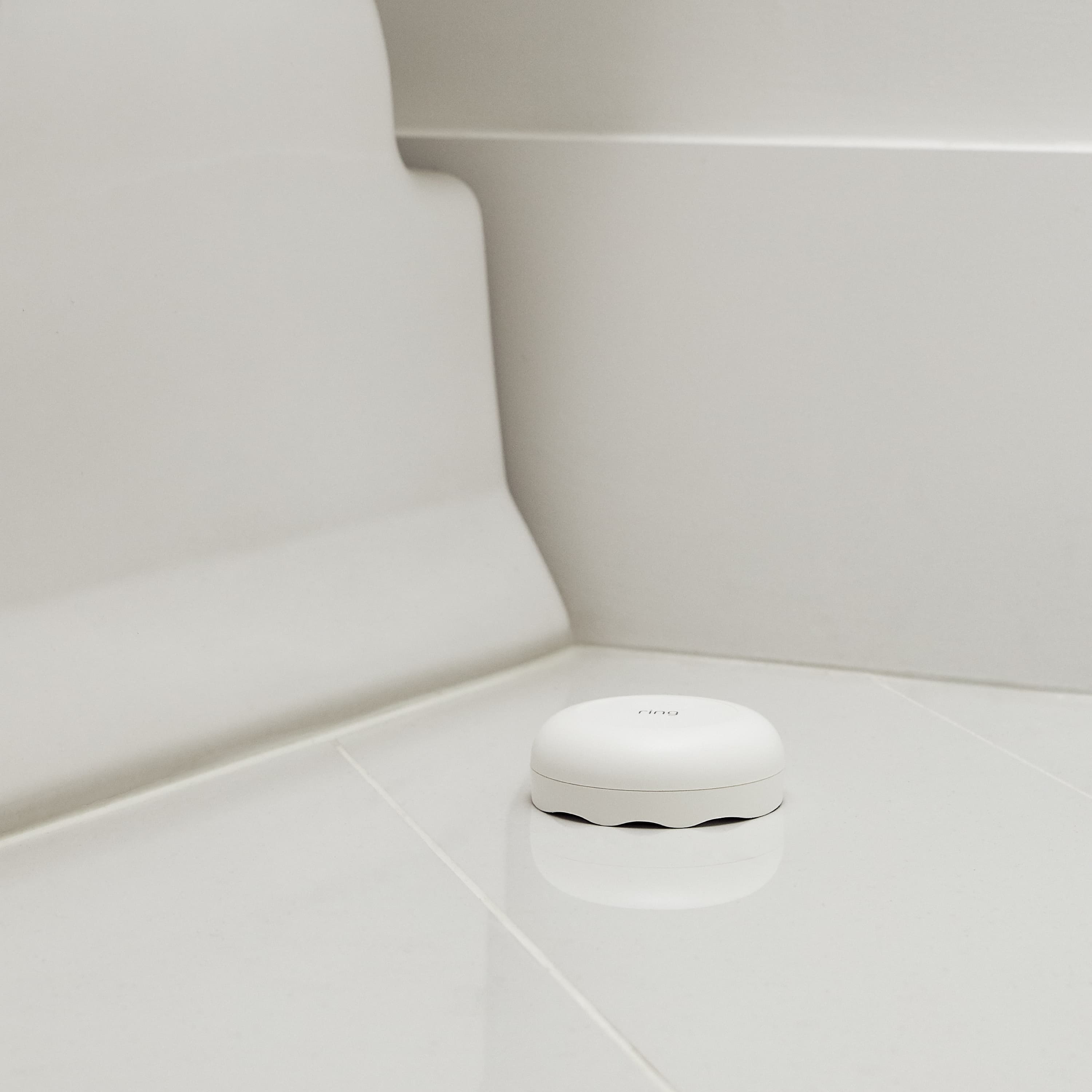 Alarm Flood & Freeze Sensor - Alarm Flood and Freeze Sensor situated on the tiled floor of a bathroom. 