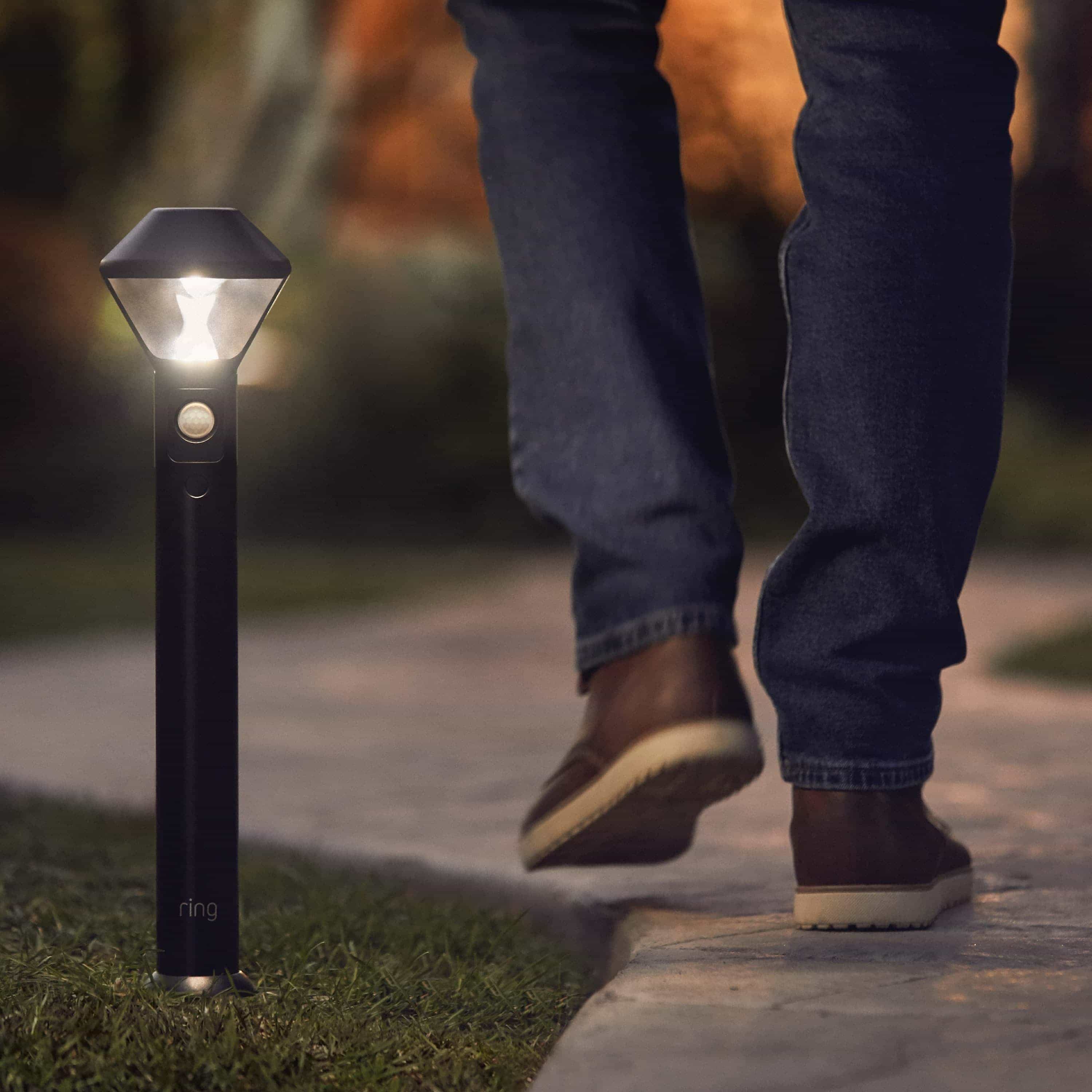 Smart Lighting Pathlight Battery - Outdoors at night, a person walks past an illuminated Pathlight Battery. 
