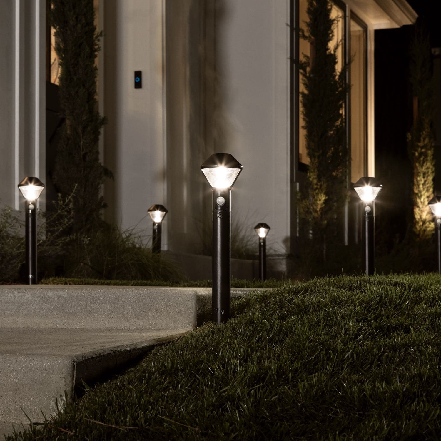 Smart Lighting Pathlight Battery - Outdoors at night, several Pathlights illuminate the walkway to the front door of a home.