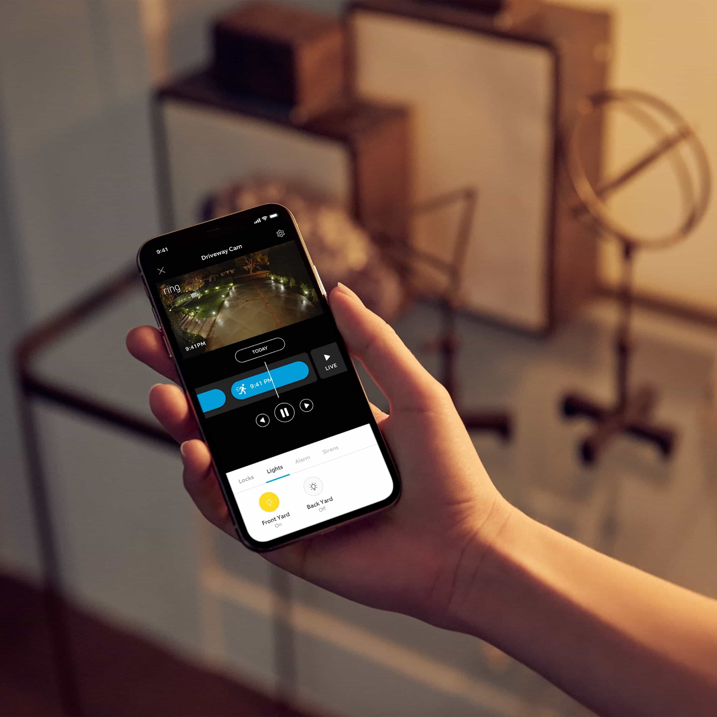Smart Lighting Spotlight Battery - Hand holding smartphone showing live video of an illuminated driveway in the Ring app.