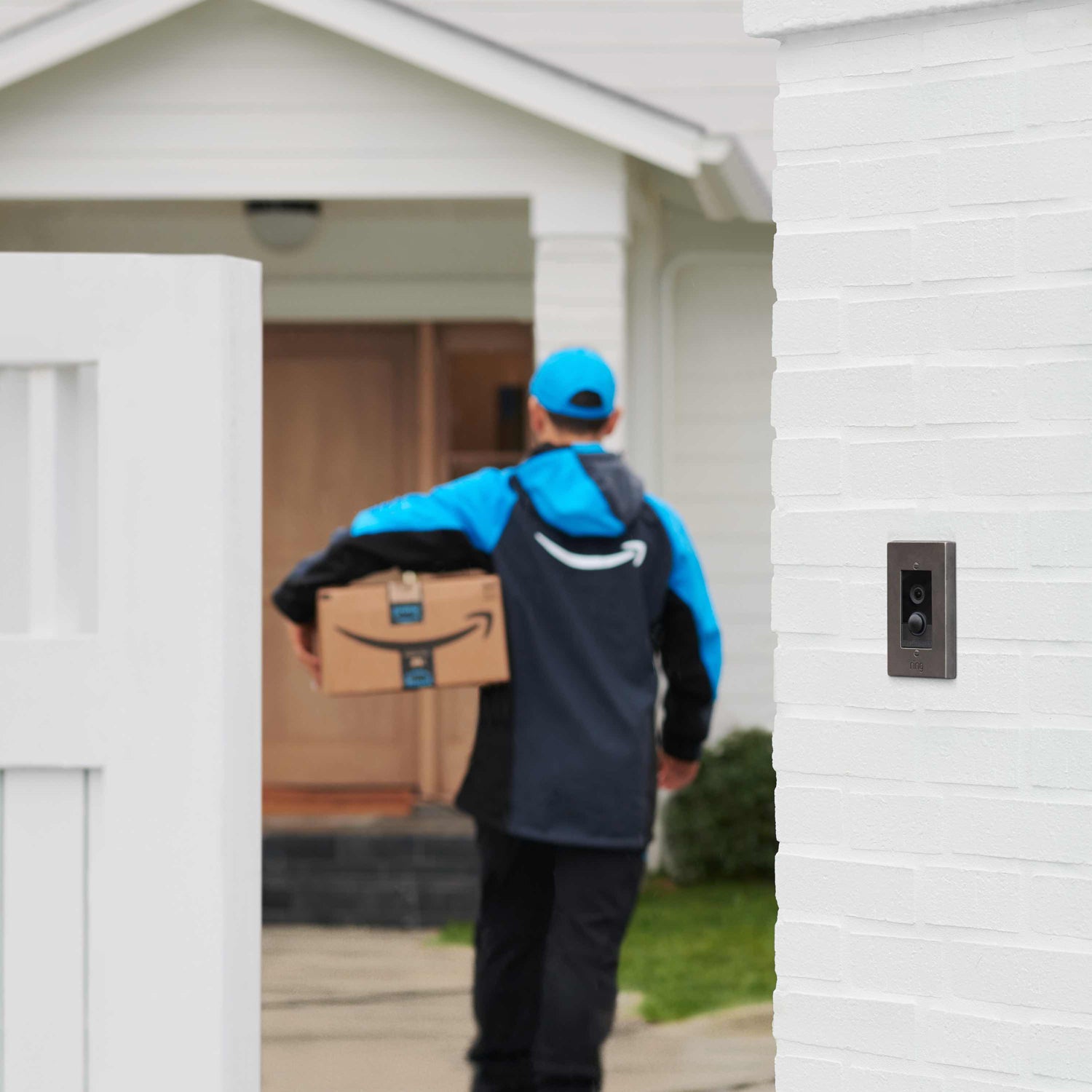 Video Doorbell Elite (Power over Ethernet) - Video Doorbell Elite mounted next to open gate. In the background, an Amazon package deliverer approaches the front door.