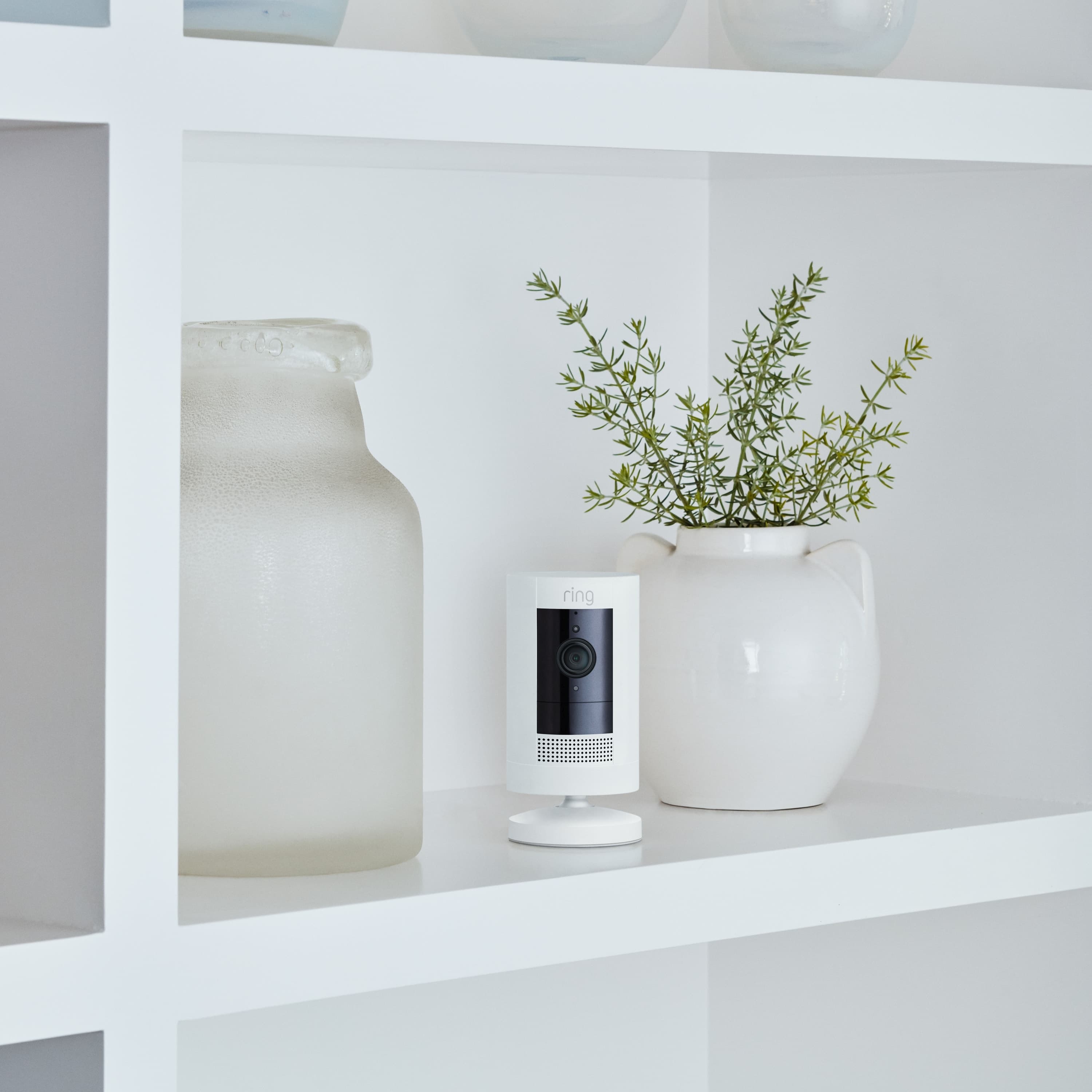 2-Pack Stick Up Cam Battery (for Certified Refurbished) - Inside a home, Stick Up Cam, Battery model in white, is situated on a shelf between 2 vases.