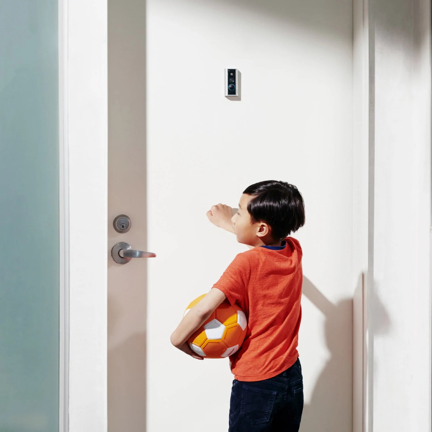 Peephole Cam (Video Doorbell) - In apartment building hallway, a child knocks on front door with Peephole Cam Video Doorbell installed.