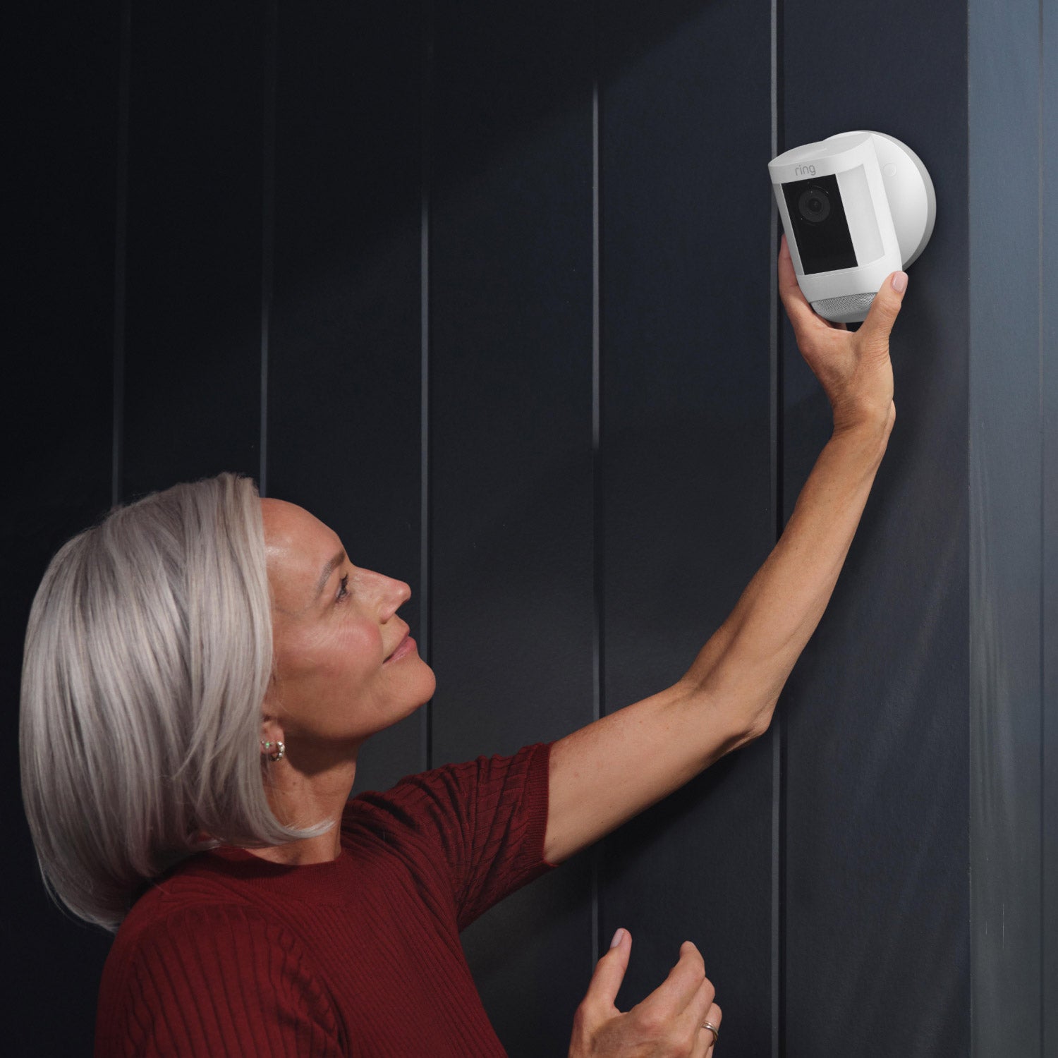 Spotlight Cam Pro (Wired) - Woman reaching up to adjust angle of Spotlight Cam Pro, Wired model, mounted on an exterior wall of home.
