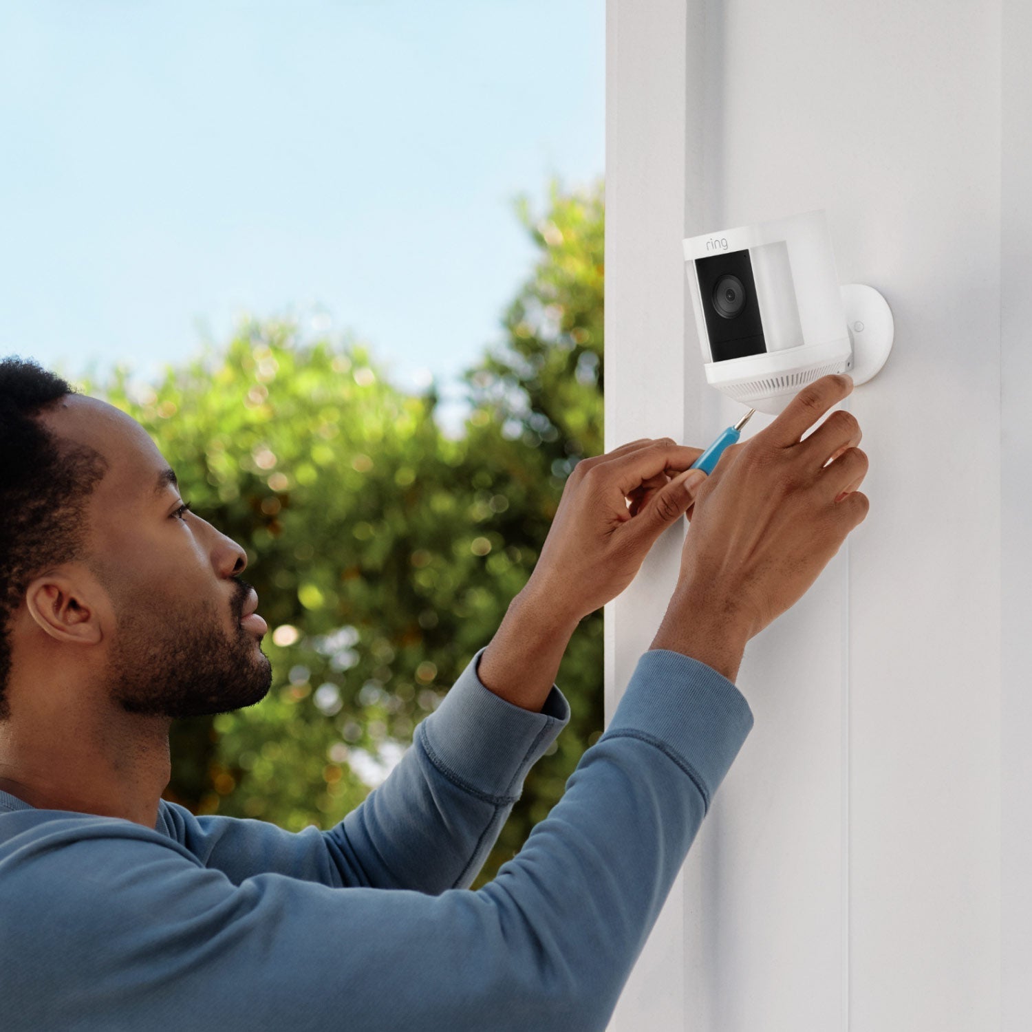 3-Pack Spotlight Cam Plus (Plug-In) - Man installing Spotlight Cam Plus, Plug-In model in white on exterior wall of home.
