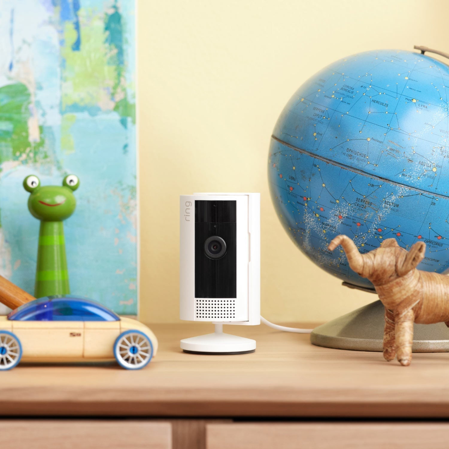 3-Pack Indoor Cam, 2nd Gen (Plug-In) - Indoor Cam 2nd Generation Plug-In model in white, situated on a kid's dresser next to a globe and some toys.