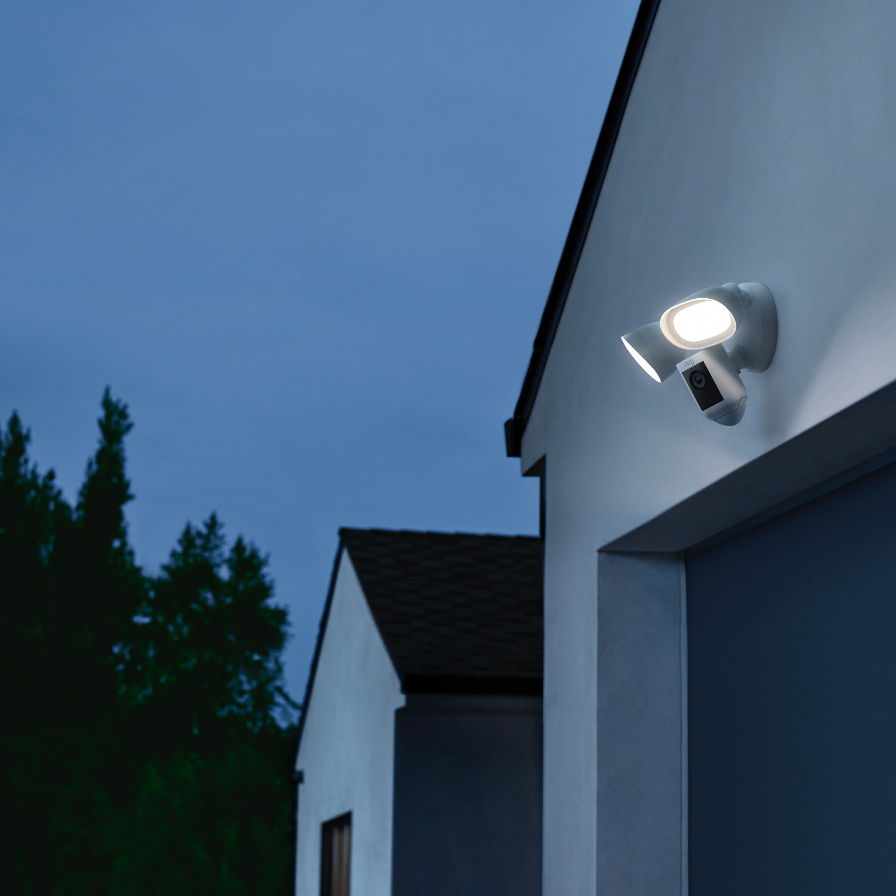 Connected Deluxe Kit (Wired Doorbell Pro (Video Doorbell Pro 2) + Floodlight Cam Wired Pro) - Outdoors at night, Floodlight Cam Wired Pro is shown mounted above garage door with both lights on.