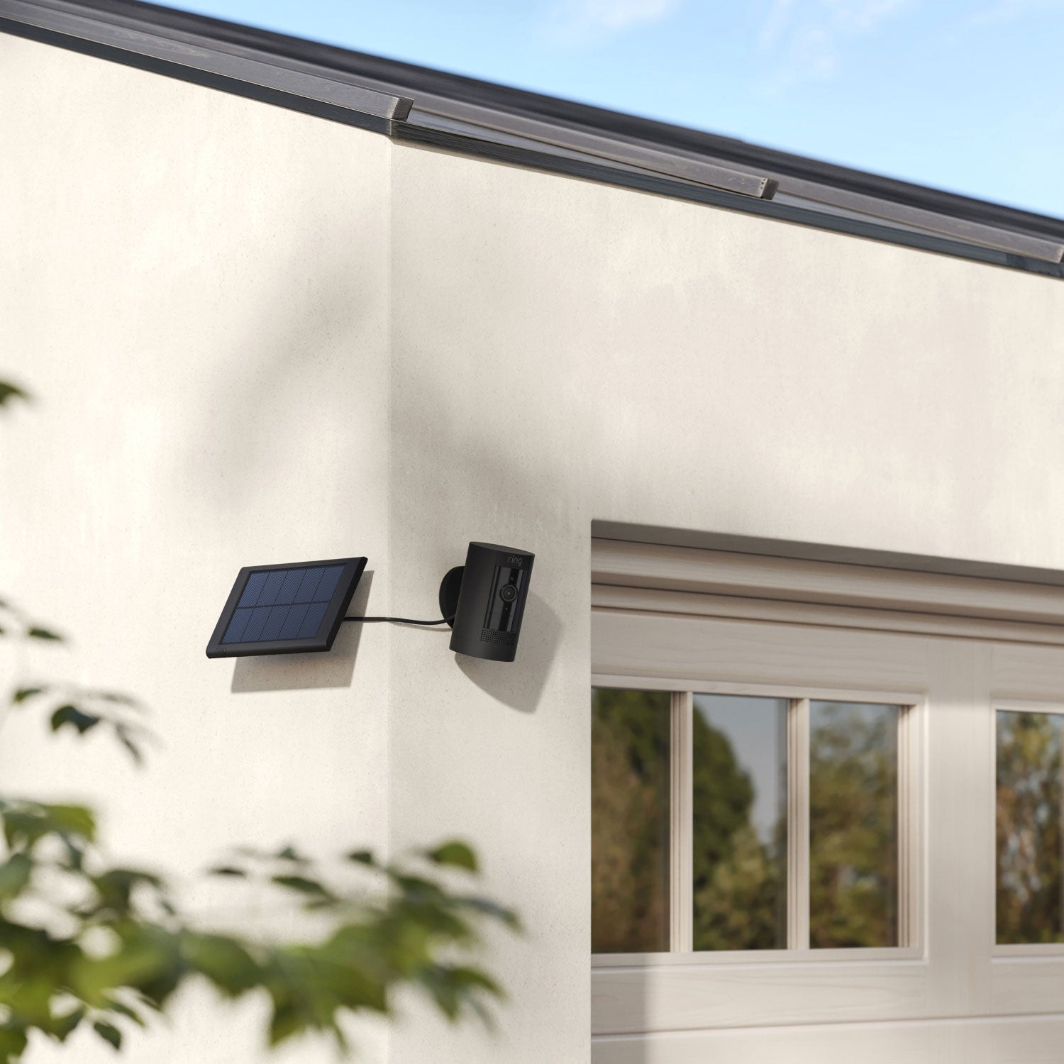 4-Pack Stick Up Cam Solar - Stick Up Cam and small solar panel, both in black, mounted to outside corner of house next to garage door.