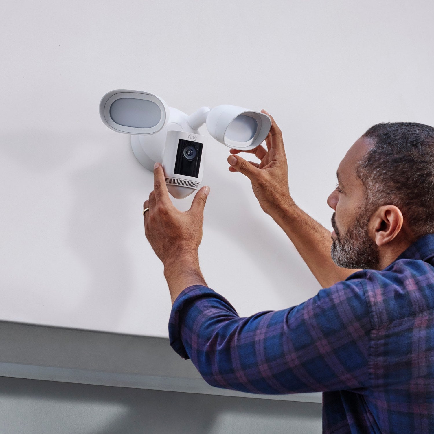Floodlight Cam Pro (Wired) - Man installing white Floodlight Cam Wired Pro on exterior wall above a door.