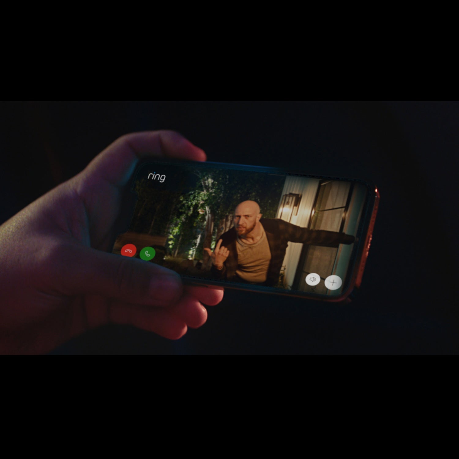 Battery Doorbell Plus - Close-up of a hand holding a smartphone. The screen shows video of a person outside a home at night, taken by a Ring camera.