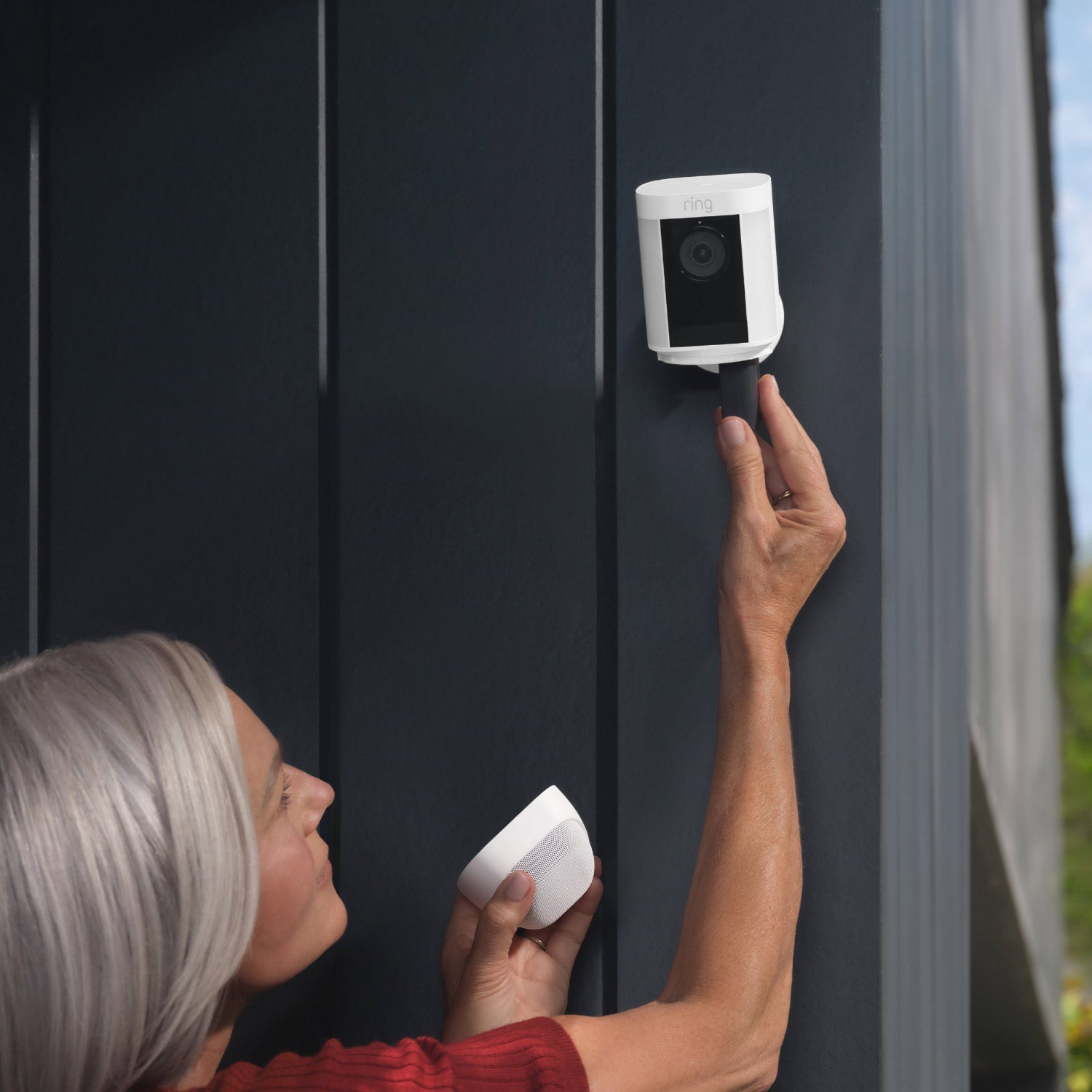 Spotlight Cam Pro (Battery) - Near the corner of a house, a woman inserts a battery pack into a Spotlight Cam Pro.