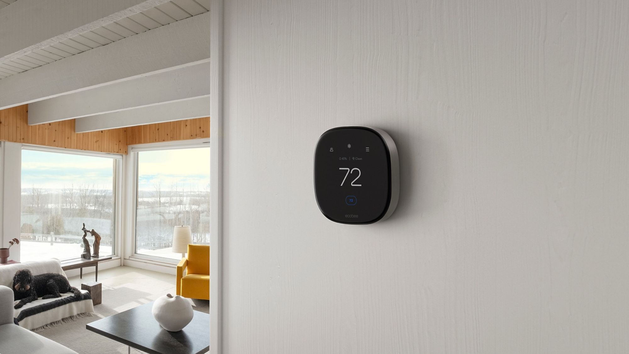 An ecobee thermostat set to 72 degrees in a modern home with lots of big windows showing the winter season outside with snow and bare trees. 