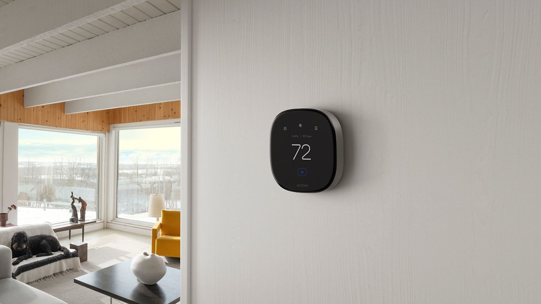 An ecobee thermostat set to 72 degrees in a modern home with lots of big windows showing the winter season outside with snow and bare trees.