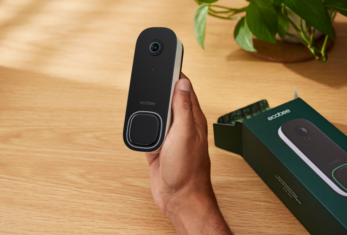 Hand holding the ecobee smart doorbell camera with the box in the background