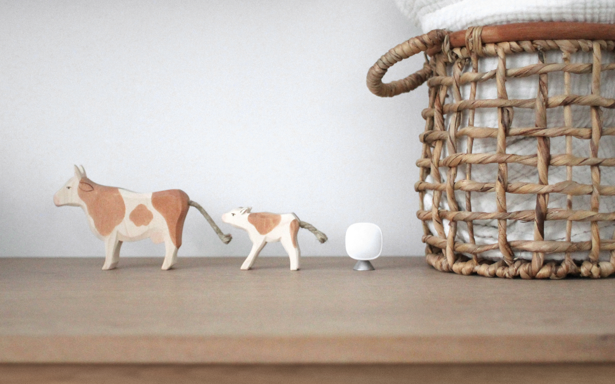 An ecobee SmartSensor sitting on a brown cabinet with two plastic animal figurines beside it and a brown wicker basket. 