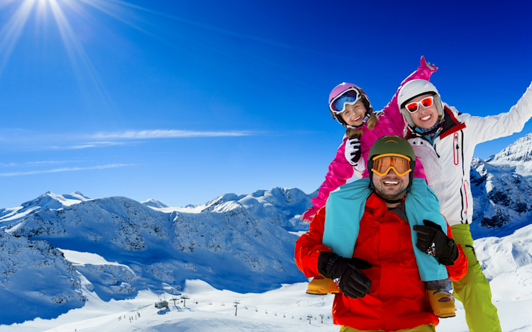 A family of three on top of the mountain ready to go skiing.