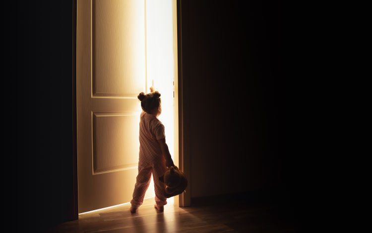 A small child holding a teddy bear opening a door.