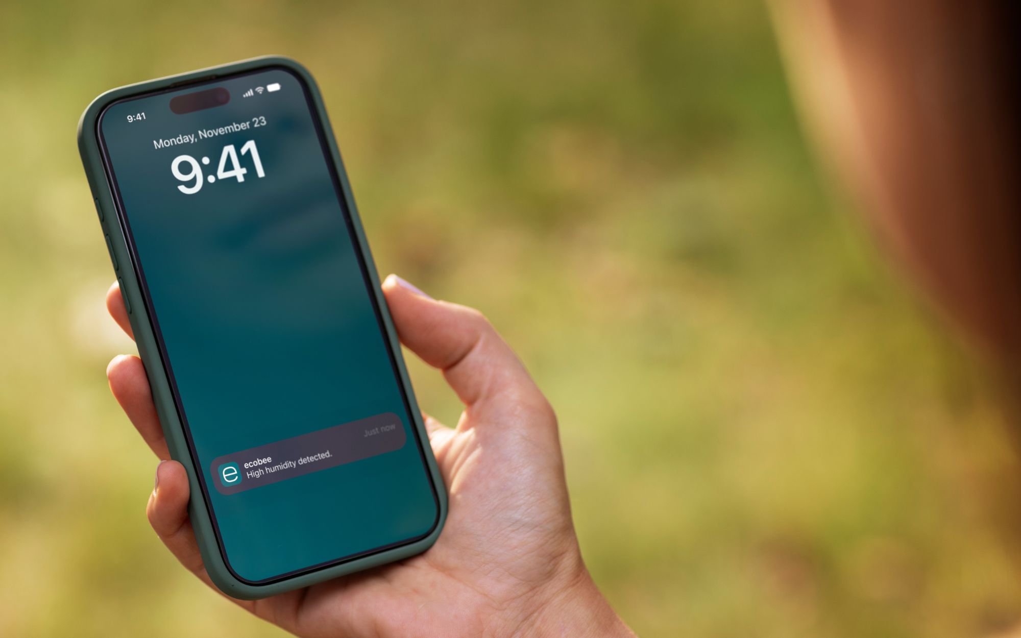 Person holding a smartphone displaying an ecobee notification alerting them to high humidity detected in their home.